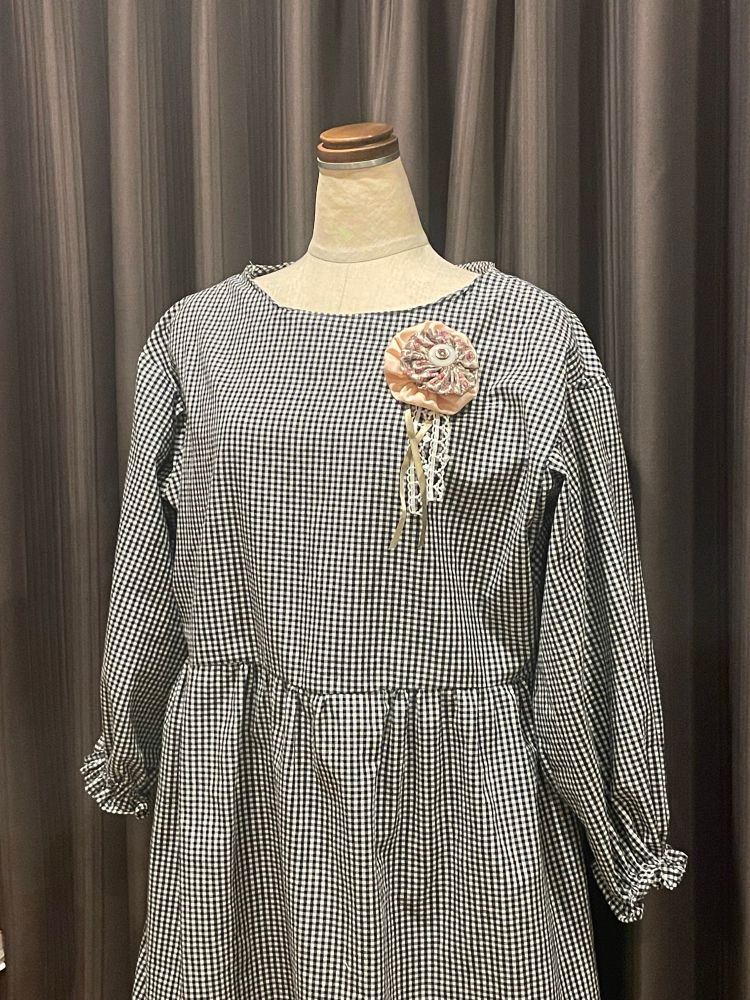 モノクロのギンガムチェックの長袖ワンピース。ピンクとレースのロゼッタ風コサージュが胸元についている。