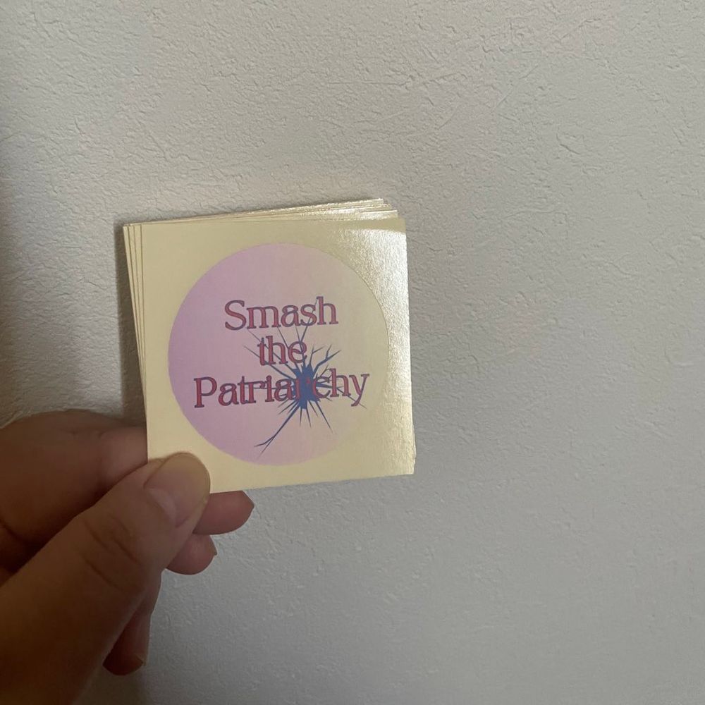 「Smash the Patriarchy」という文字の入った丸いピンクのステッカー。ひび割れの模様が入っている。