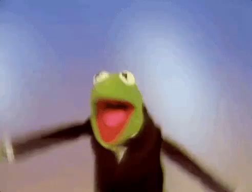 kermit the frog is wearing a tuxedo and flying through the air with his arms outstretched .