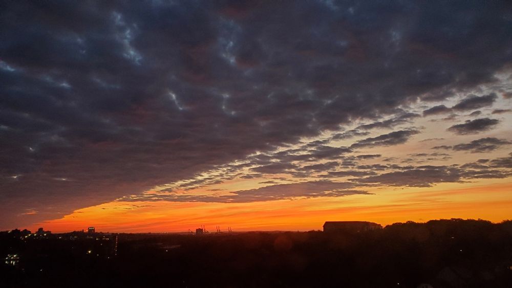 A picture of sunrise. Vibrant reds, oranges, and yellows, cut by a sharp diagonal line of clouds, with the silhouette of Southend Halifax at the bottom.
