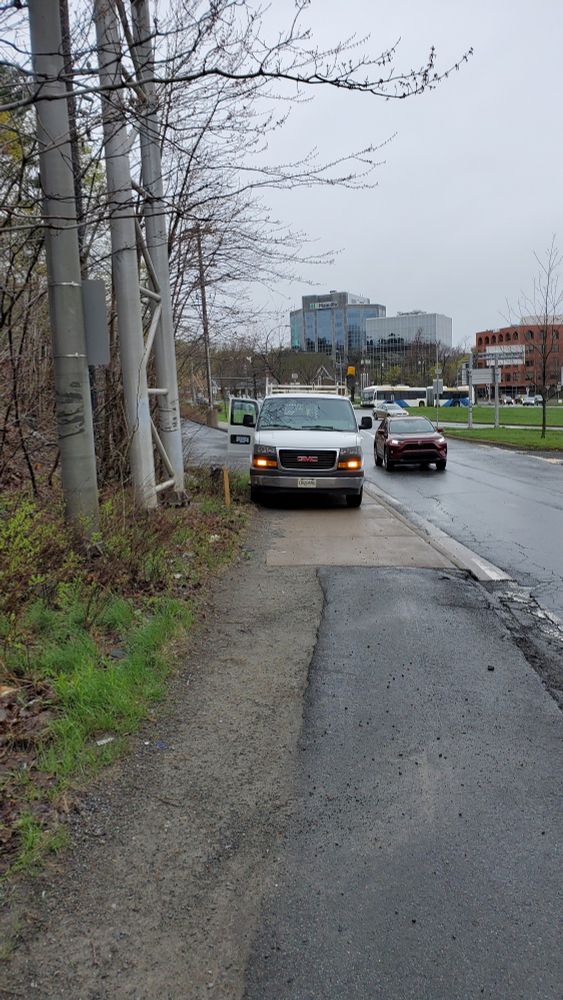 A white van parks on the sidewalk forcing people to walk in the street to get by.