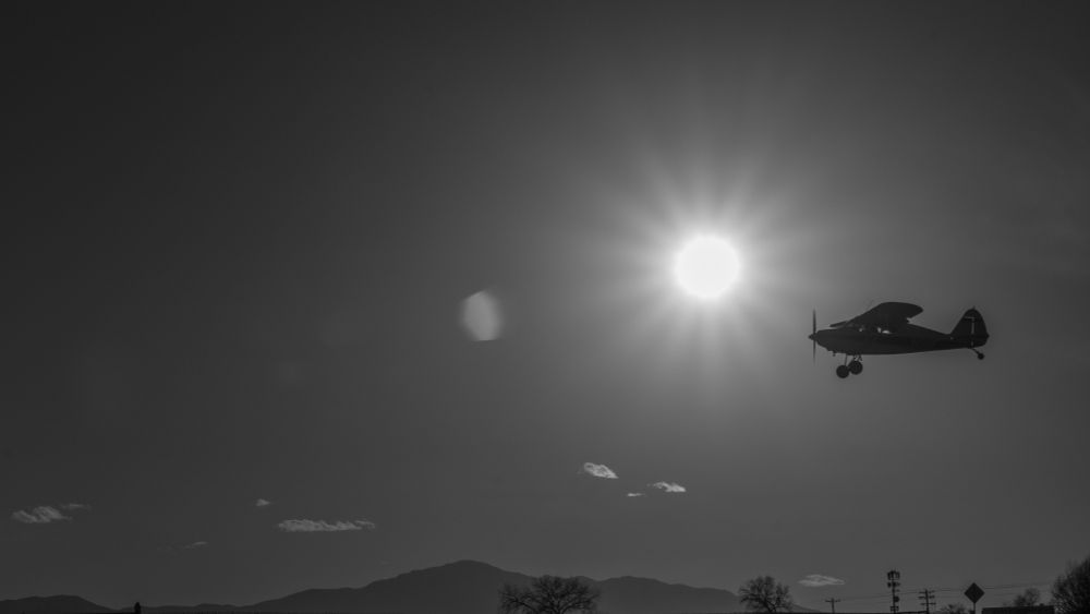 Black and white photo of a plane landing with the Rocky Mountains and the sun in the background
