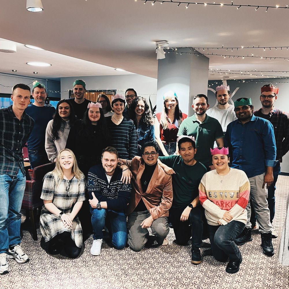 Members of the Hive IT came together for a group photo and stood in front of a grey wall wearing different coloured party hats.