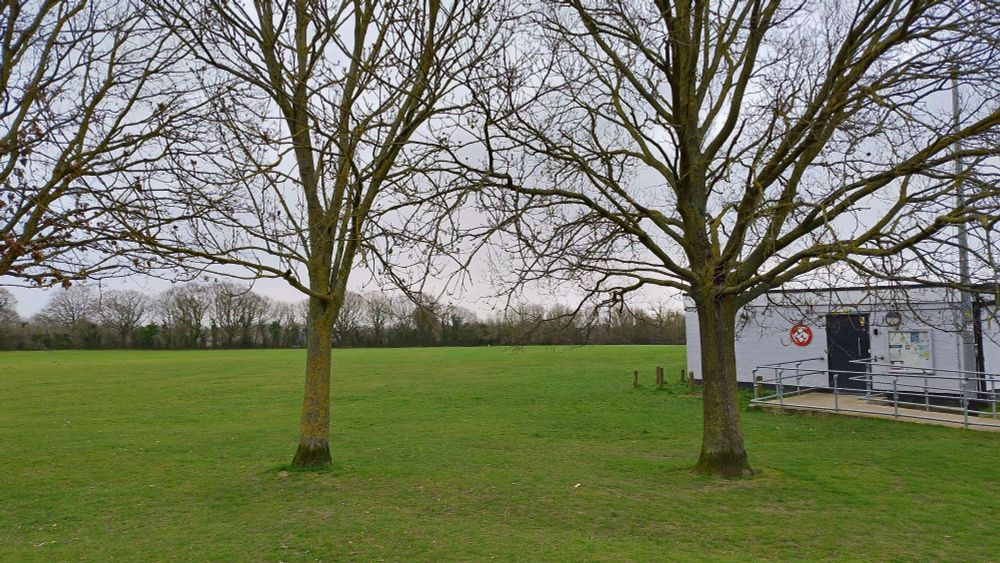 A view of the Hackspace building which is squat and bunker-like. It's on the edge of a large grass field and the trees are yet to leaf.
