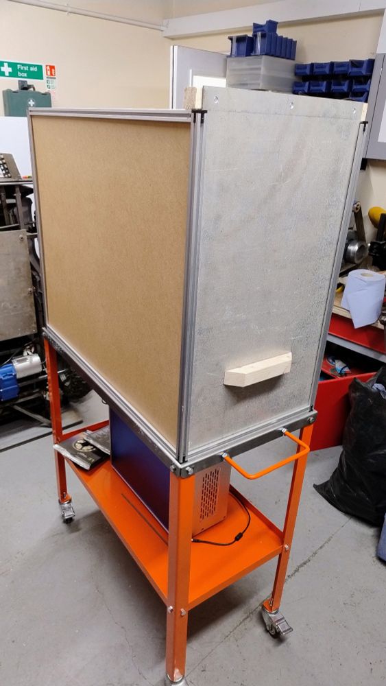 A large enclosure made from 2020 extrusion and board. There's a hatch in the front with a rudimentary handle to slide it up.