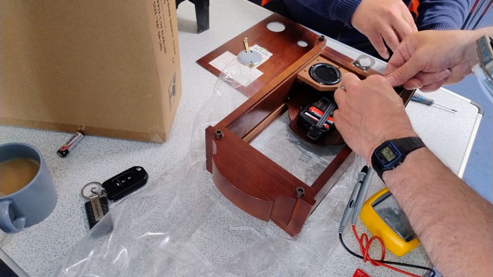 The insides of a wooden clock with the connections being checked with a multimeter.