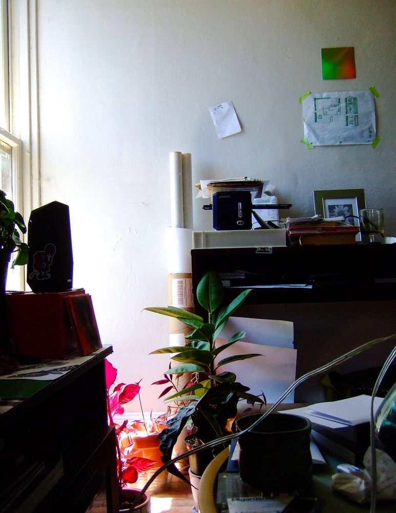 Of my living space heres my tv stand on the left, some plants cooped up in a corner by the window. My coffee table with a miscellaneous of things, and my desk carrying my film scanner, film, and a photo frame in sight. The wall has an idea of a show layout i wanted to do