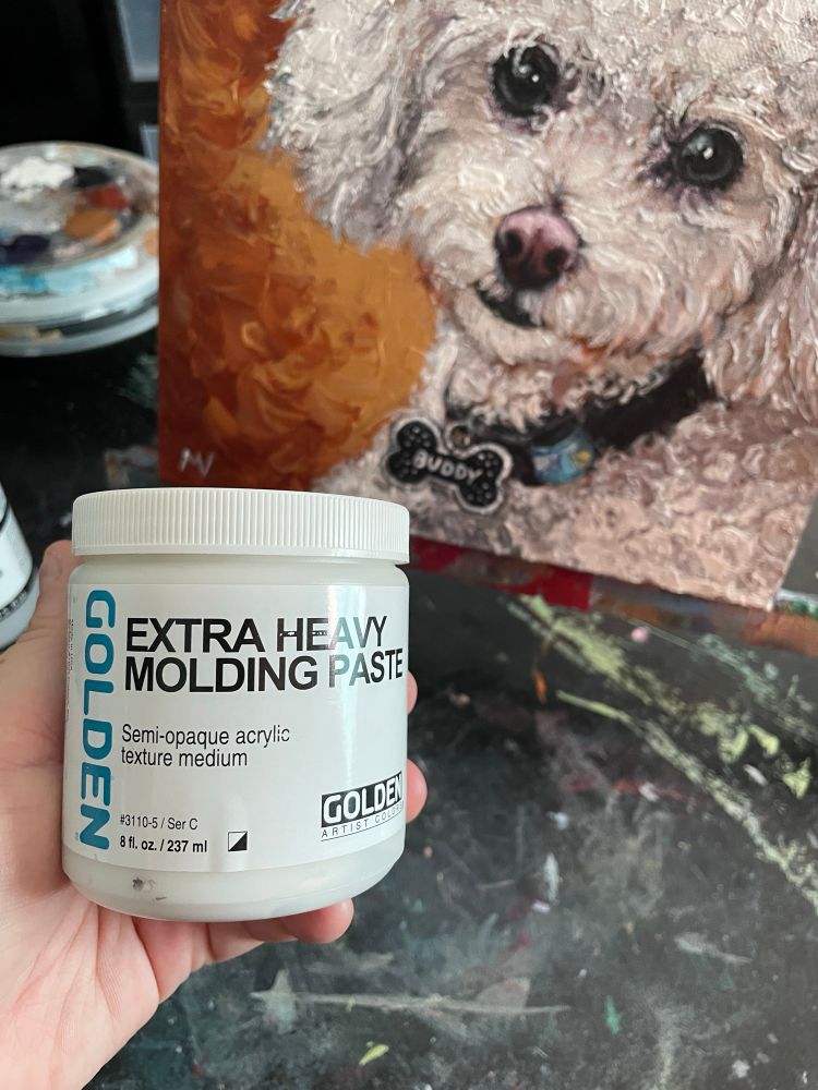 Photo of hand holding container of Golden brand extra heavy molding paste, in front of a painting of a dog on an easel. The dog is fluffy and white with a tag that says "buddy," and the background is reddish brown. Pet portrait by New Orleans artist and illustrator Melissa Vandiver. #dogs #dogsky #dogsofbluesky