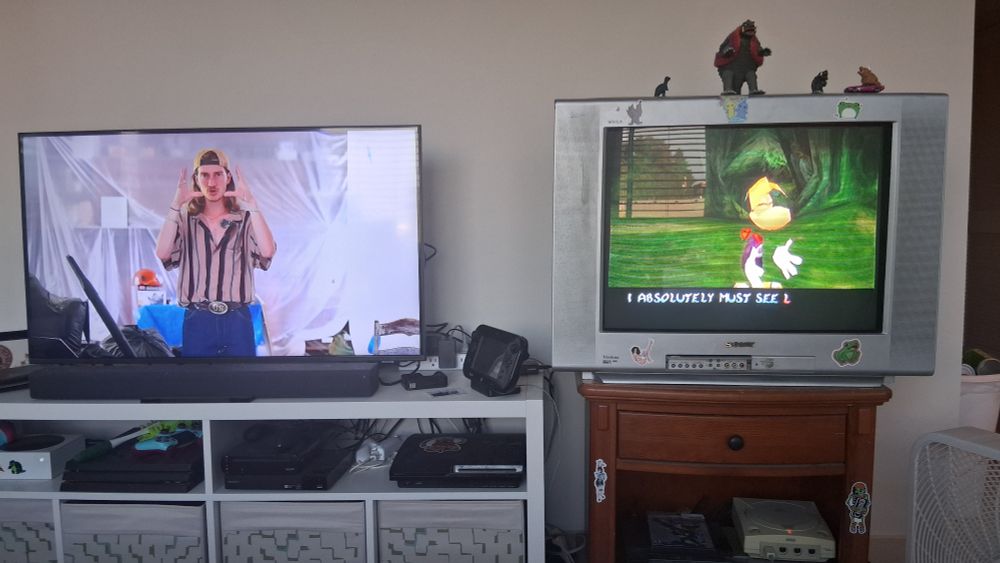 Two televisions, one showing milo rossi holding his hands up near his face. The other is a crt playing Rayman 2 from the dreamcast. Rayman holds his hands like milo. Conspiracy confirmed.