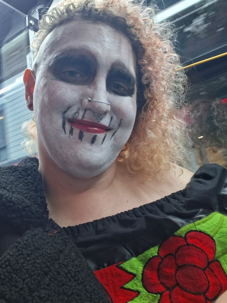 Me in white and black skull face paint. Curly.hair and you can see a bit of my black dress with red rose embroidery 