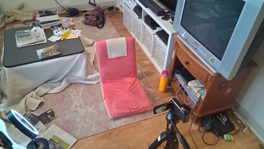 Pink floor chair with a camera facing it and small light off to the side and just TONS of clutter all around me