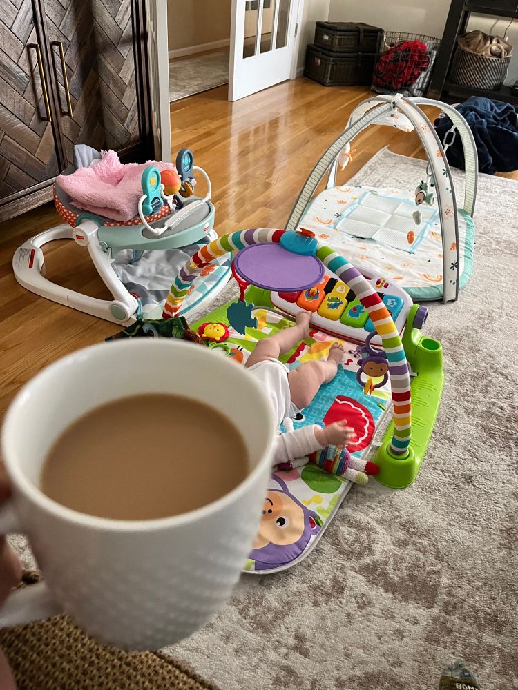 Milky coffee in white mug. A baby is on a play mat in the background.