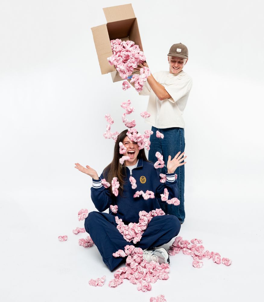 Po dumping a box full of pink scrunchies on Paige's head, as Paige sits on the ground with her hands up