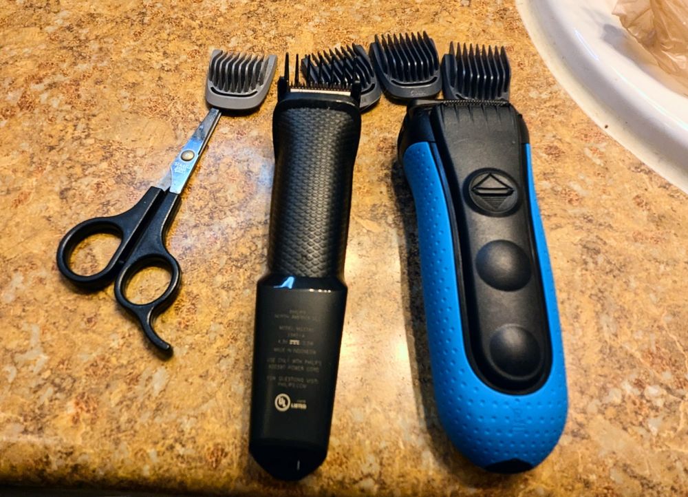 Various hair maintenance implements. Fine scissors, a trimmer with different length attachments, and a blue handles shaver. 