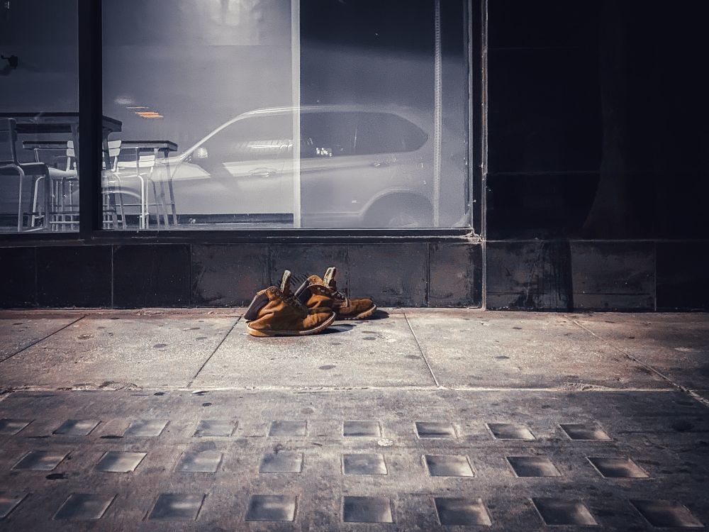 A pair of worn out old Timberland boots are being photographed on the sidewalk in Downtown Los Angeles. The boots appear to have been stepped out of while walking (mid-stride). While not unusual to see one shoe in the middle of the sidewalk or street, it is unusual to see a pair of boots untouched by others on the street, almost as a ghost left them behind. 