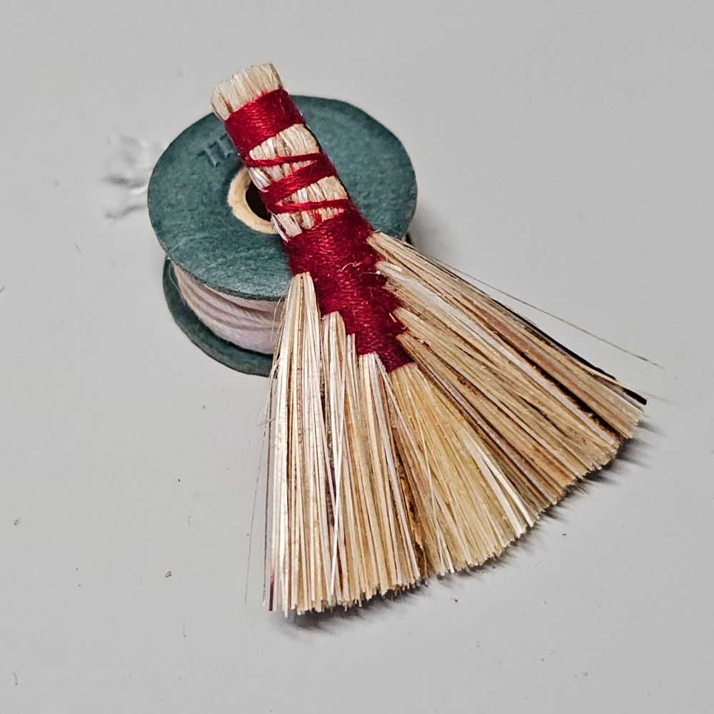 1:12 scale broom with red stitching resting on a paper bobbin.