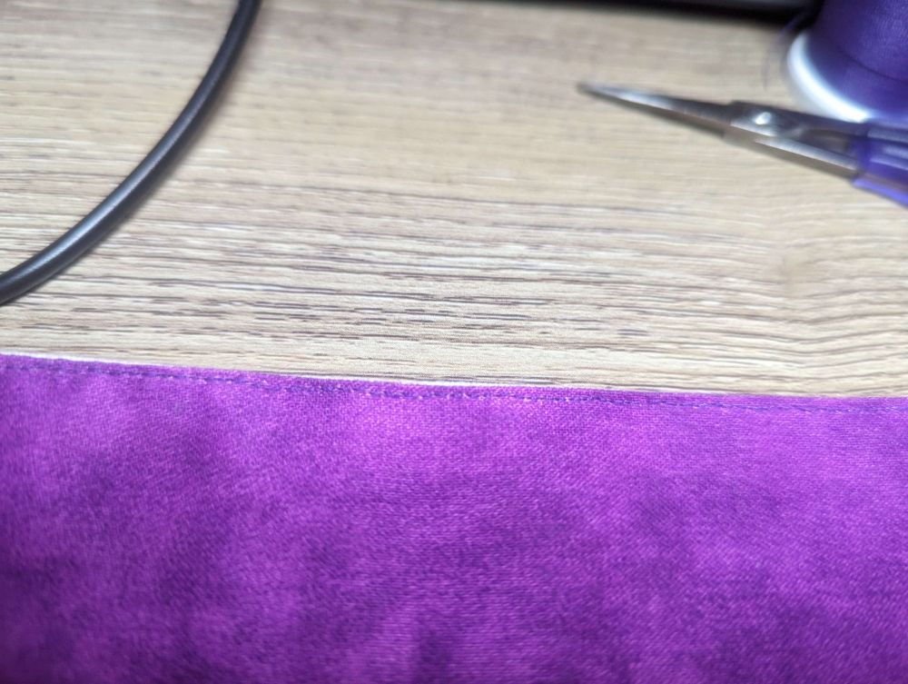 Purple fabric sitting on a desk with a precise hand stitched top stitch at the edge.