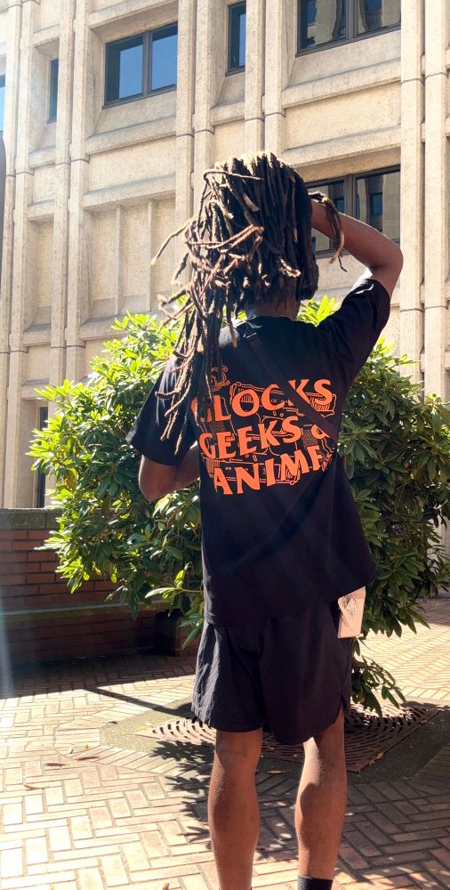 posing like cloud in front of shinra tower. im holding my locs up to bring my graphic image on the back of my shirt into view. its a black shirt that read "glocks geeks and anime"