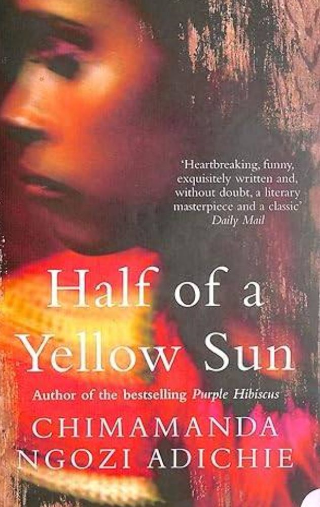 Book cover for Half of a Yellow Sun by Chimamanda Ngozi Adichie. The text is in white, and the illustration is of yhe face of a black woman in profile with her gaze downwards, with red and yellow lighting behind her