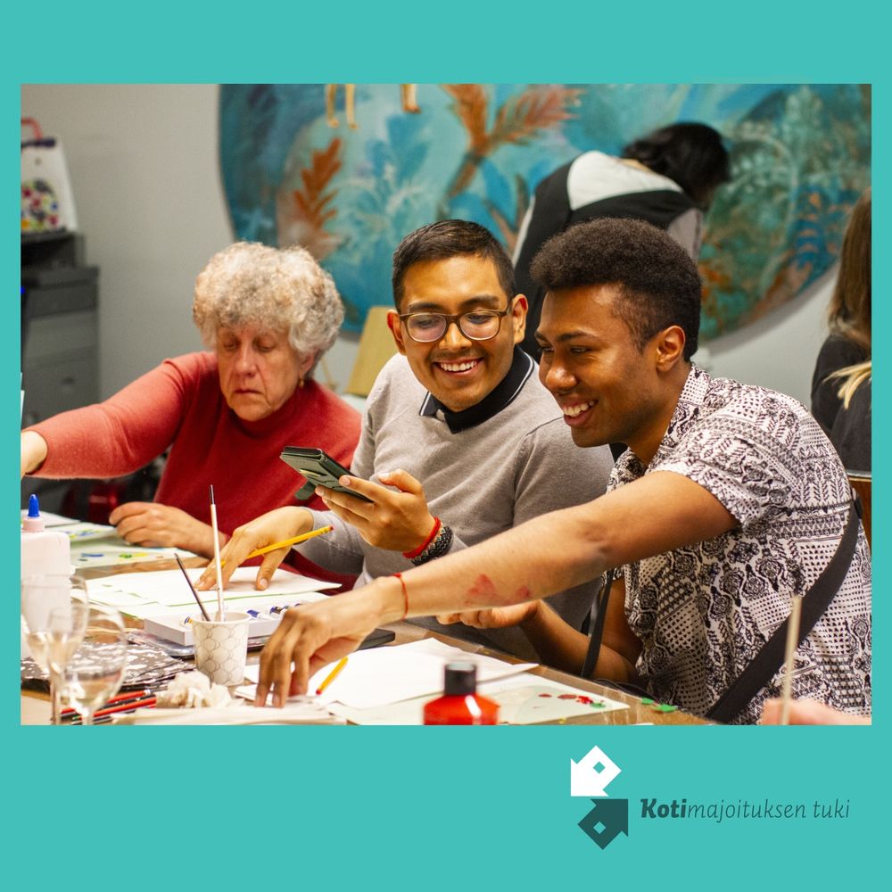 Kuvassa kolme ihmistä, josta kaksi etualalla olevaa hymyilee