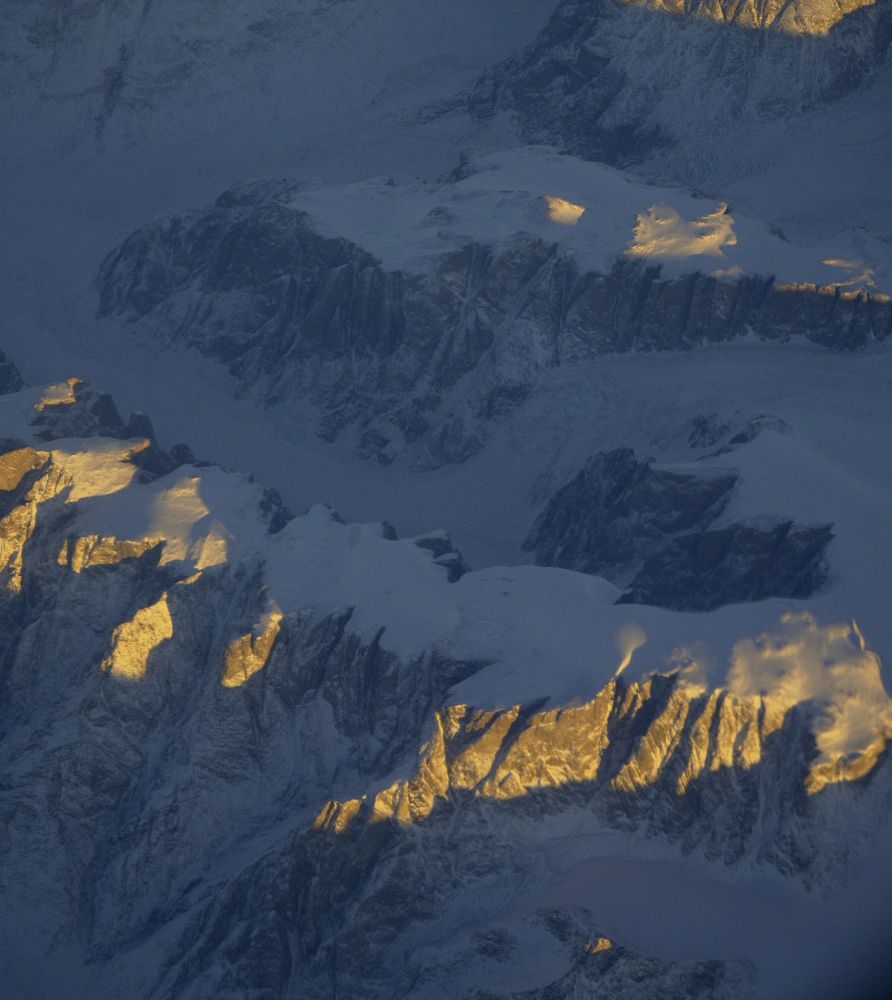 Image of flat topped rocky mountains covered with snow and lit by the sun.
