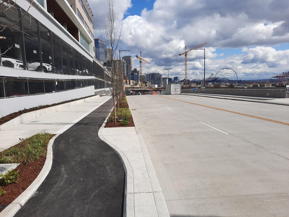 Elliott Way in Seattle facing southeast. there is a protected bike lane on both sides of a four lane stroad. no shade in sight.