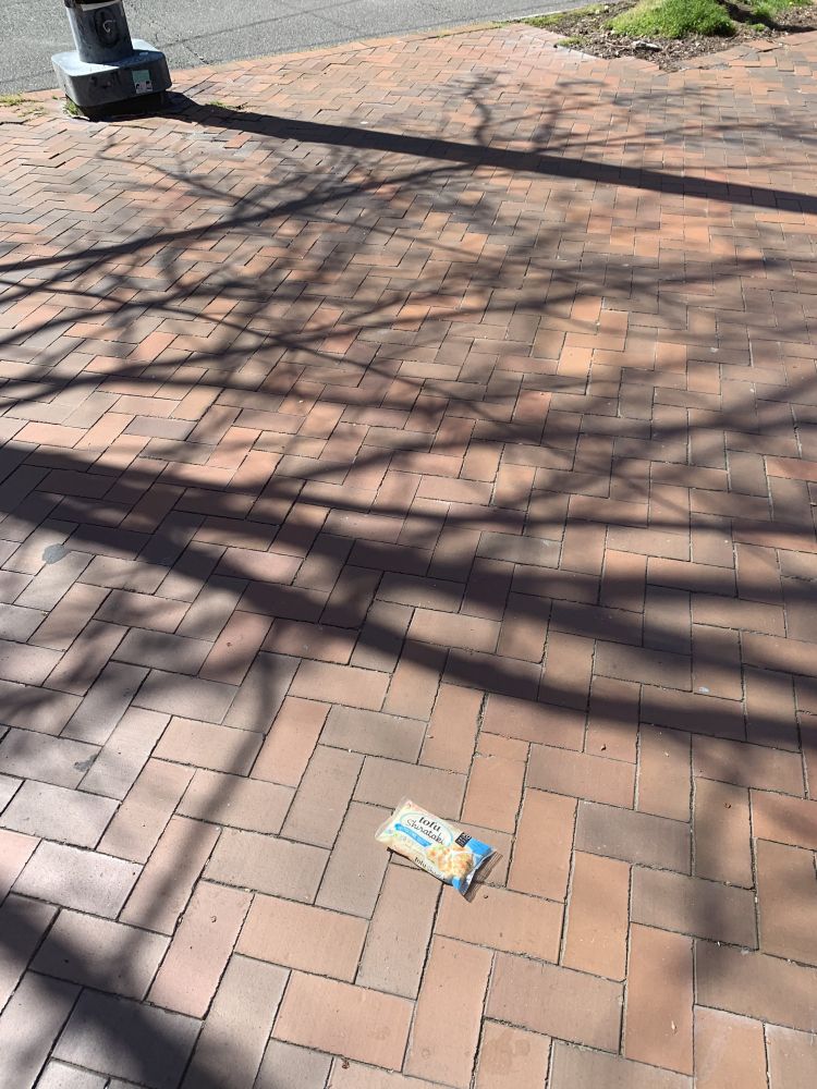 an unopened package of tofu shirataki noodles on the ground, which is a zig-zag brick pattern