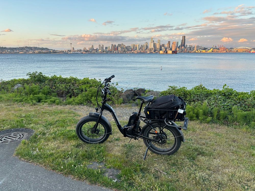a black folding e-bike in front of Elliott Bay with the Seattle skyline in the background at sunset 