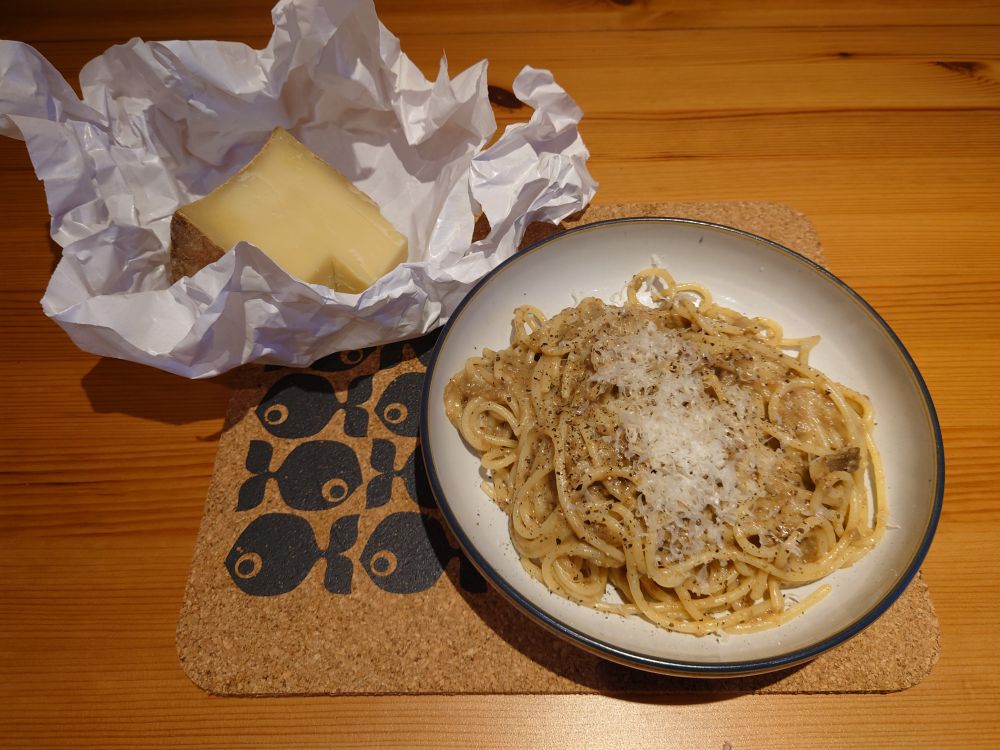 large wedge of cheese in paper wrapping and a bowl of spaghetti ai funghi