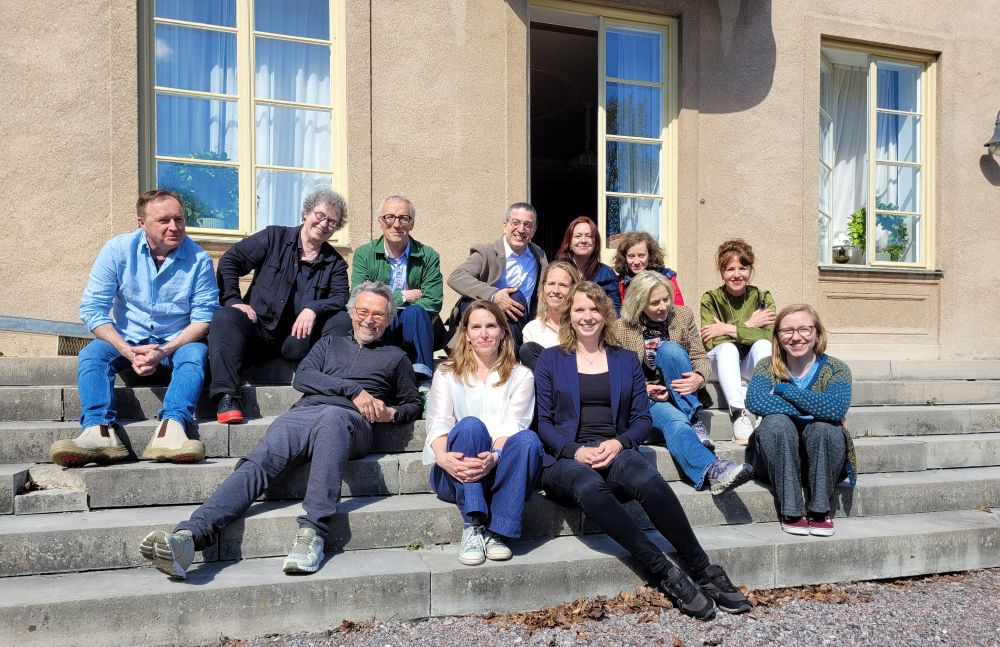 Researchers sitting on steps at the back of a large house, smiling in the sunshine for a group photo. 
