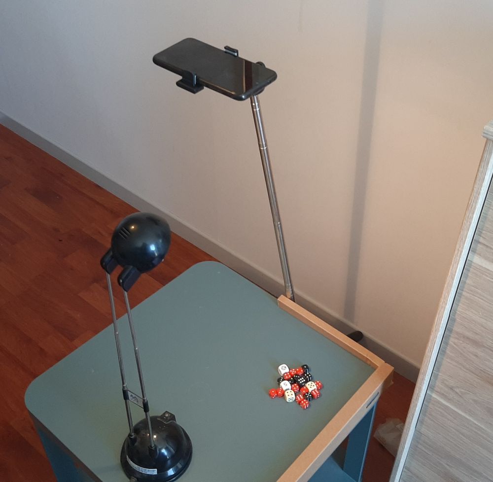 Une petite table basse avec des dés dessus. Un smartphone sur un pied filme la table basse
