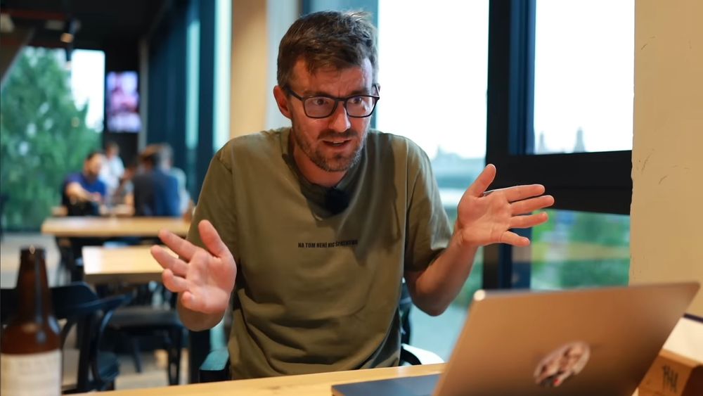 Screenshot of a video, presented by Janek Rubeš, sat at a pub table, with three blurry figures in the background.