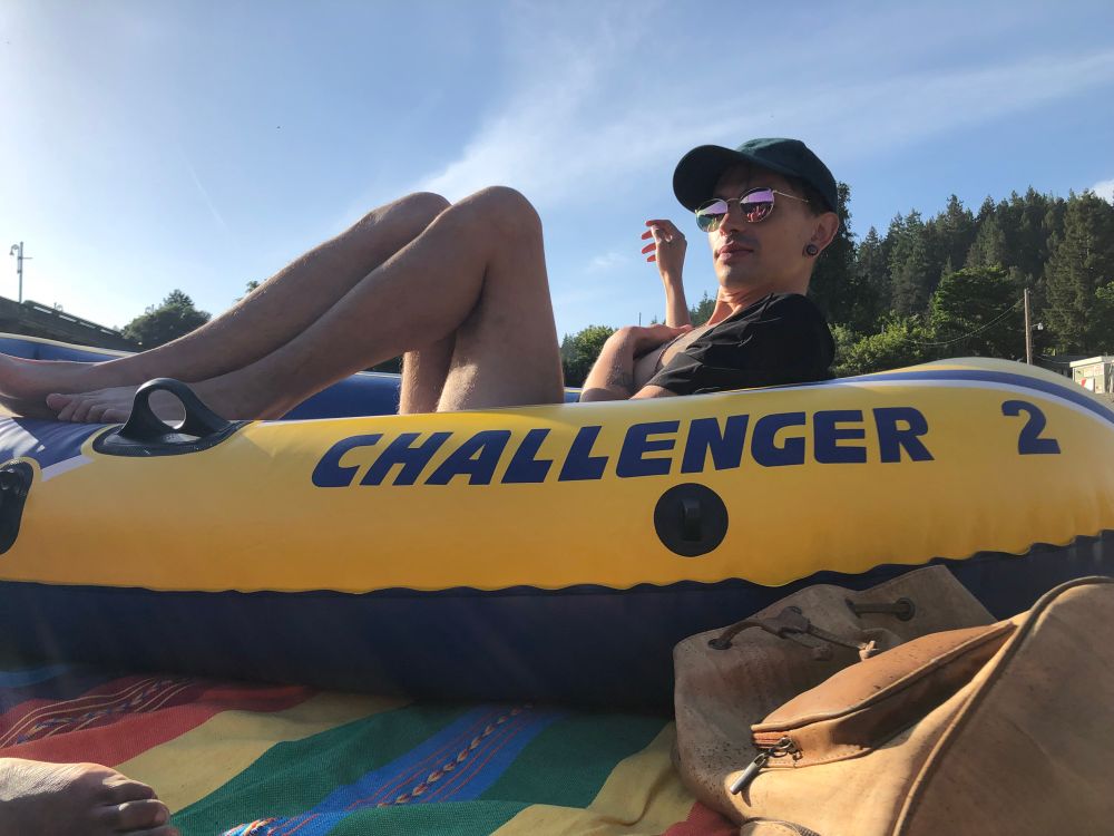 Gay person lounges in an inflatable raft with the title “Challenger 2” on the side of it