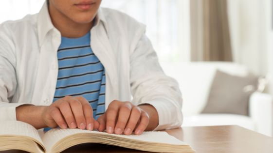 Person reading a book in braille at a table indoors.