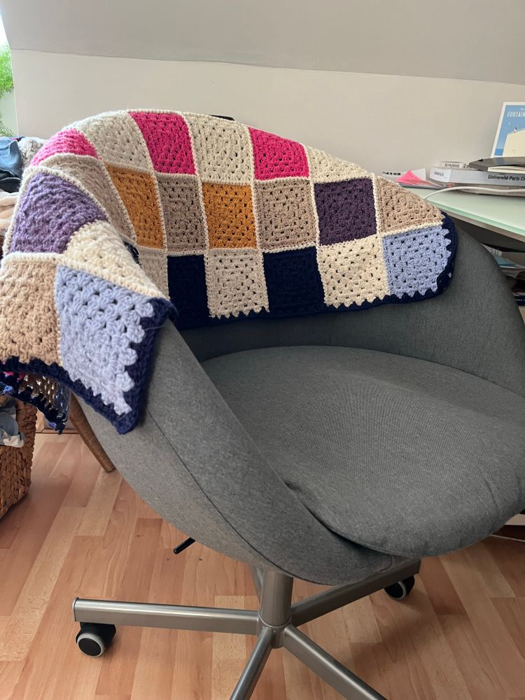 chaise de bureau format club gris en tissus avec une couverture en granny square multicolores en crochet posées dessus
en arrière plan on voit mon bureau et le mur en appentis