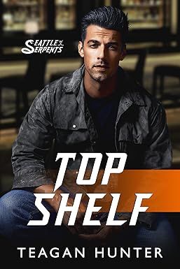 The book cover for Top Shelf by romance author Teagan Hunter. It shows a handsome white man looking straight ahead. He has black hair and a chin dimple and is wearing a black jacket and jeans.