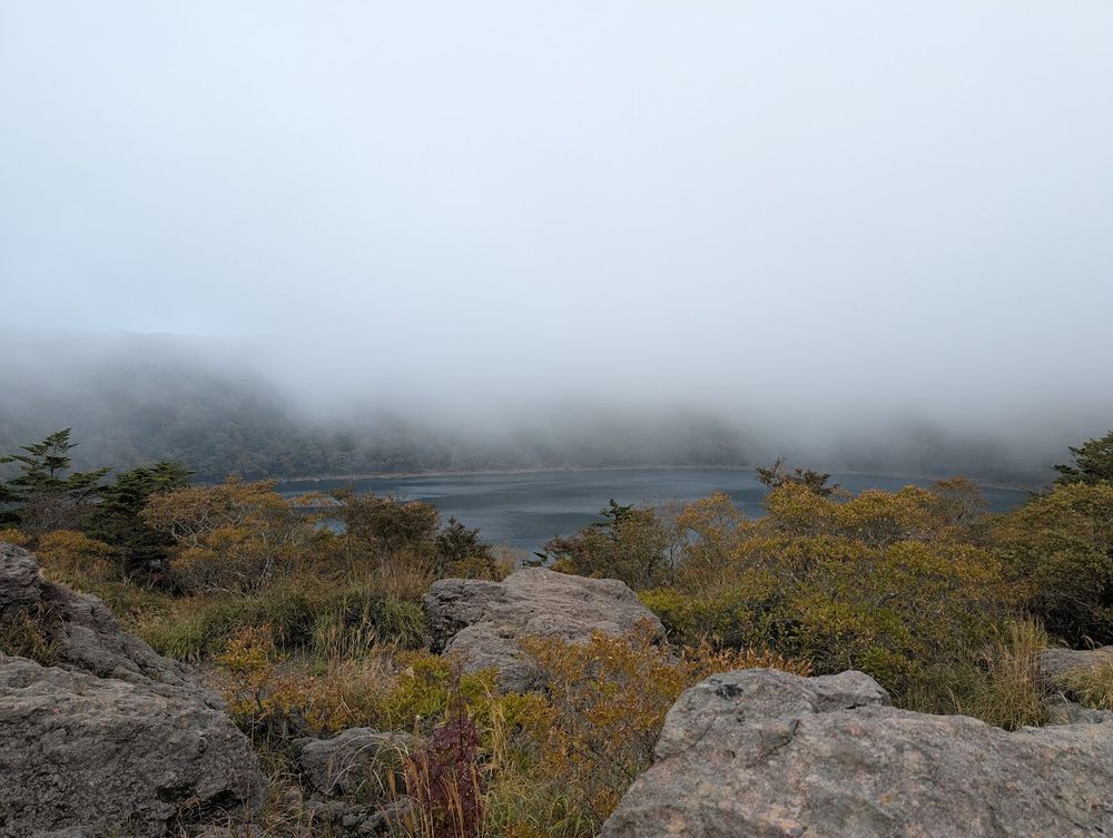 a low mountain fog, over a sparkling blue lake, with autumn coloured leaves on scrubby bushes growing on the volcanic soil
