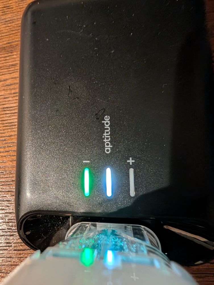 Aptitude Metrix COVID test results showing negative result: green negative light and white power light, on a hotel room wood grained desk 