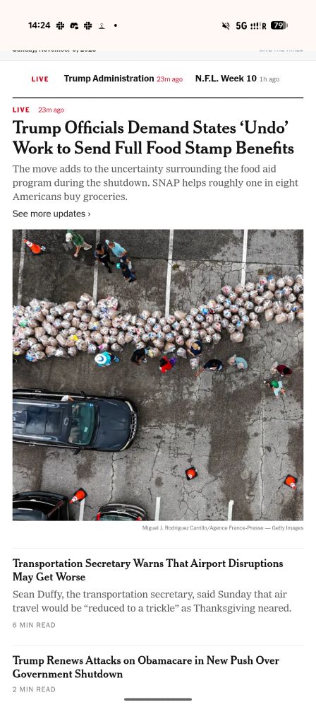 A mobile news webpage screenshot from The New York Times, dated Sunday, November 9, 2025, showing at 14:24. The page displays several news stories under "LIVE" coverage with "Trump Administration 23m ago" and "N.F.L. Week 10 1h ago" tabs at the top.

Main headline (LIVE, 23m ago): "Trump Officials Demand States 'Undo' Work to Send Full Food Stamp Benefits"

Subheading: "The move adds to the uncertainty surrounding the food aid program during the shutdown. SNAP helps roughly one in eight Americans buy groceries."

Below is a link reading "See more updates ›"

The main image shows an aerial photograph of people queuing alongside numerous white bags or sacks arranged in rows on cracked pavement, with vehicles visible including a dark-coloured van. Photo credit: "Miguel J. Rodriguez Carrillo/Agence France-Presse — Getty Images"

Second story headline: "Transportation Secretary Warns That Airport Disruptions May Get Worse"

Subheading: "Sean Duffy, the transportation secretary, said Sunday that air travel would be 'reduced to a trickle' as Thanksgiving neared."

Time indicator: "6 MIN READ"

Third story headline: "Trump Renews Attacks on Obamacare in New Push Over Government Shutdown"

Time indicator: "2 MIN READ"