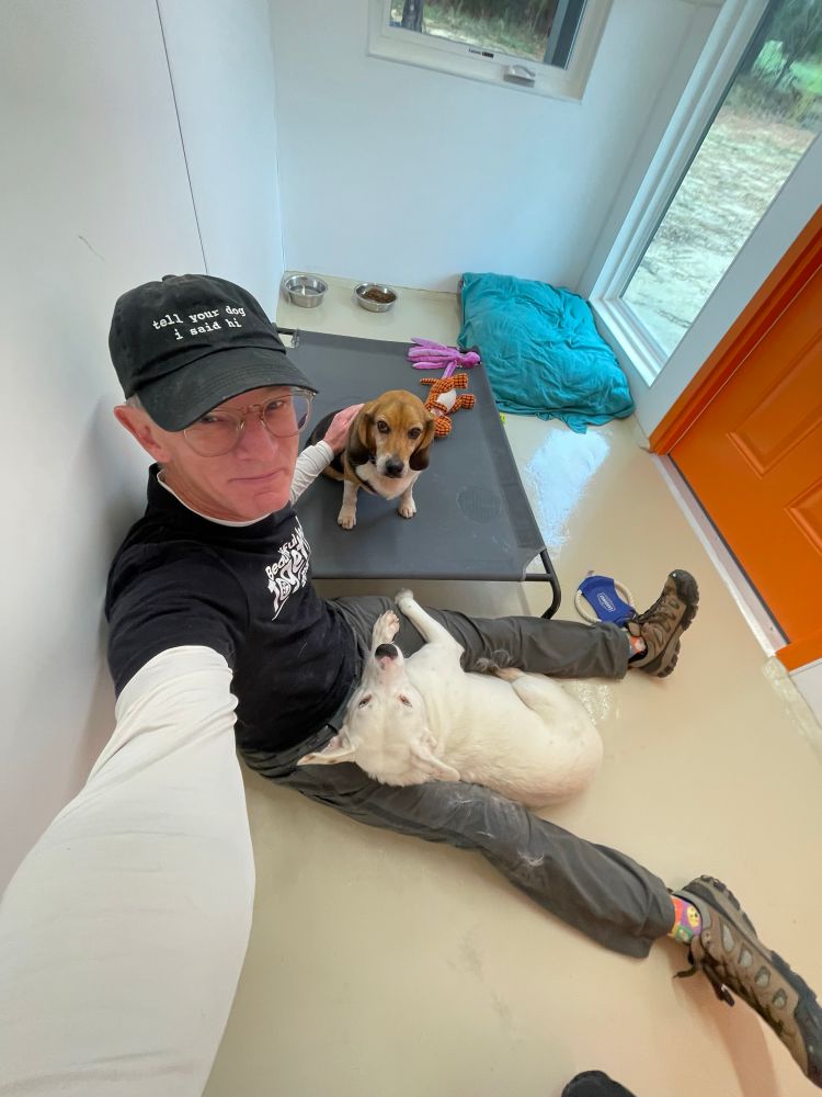 A man sitting on the floor with the white dog in his lap and the beagle sitting next to him