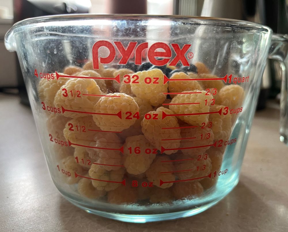 Four cups of yellow raspberries in a Pyrex cup with a few blueberries on top