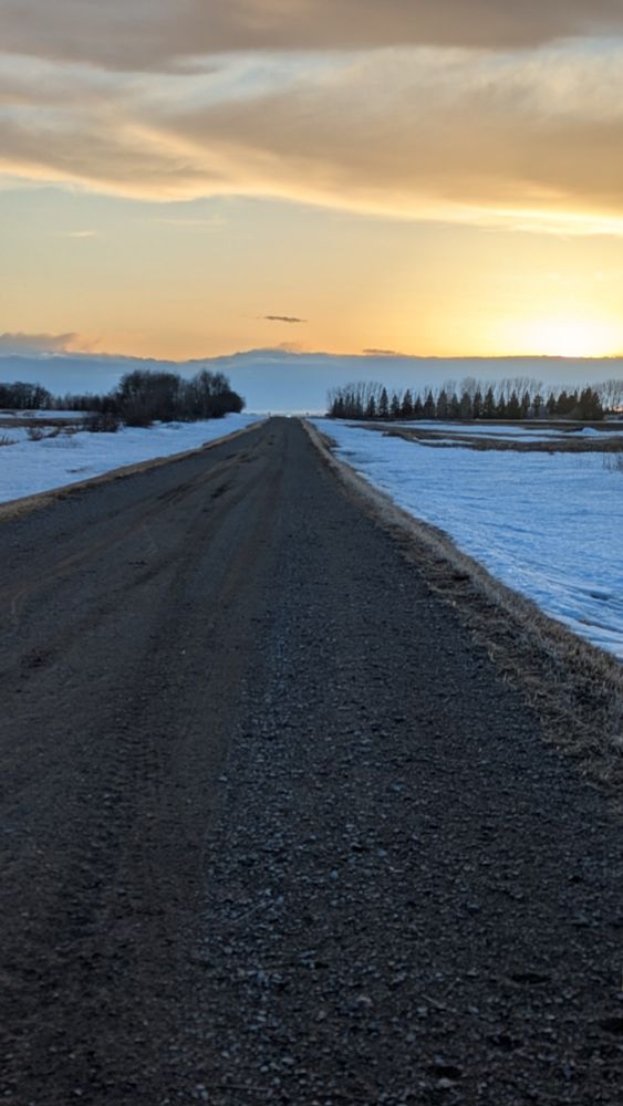 Sunset on a gravel road. The fields are covered in snow.