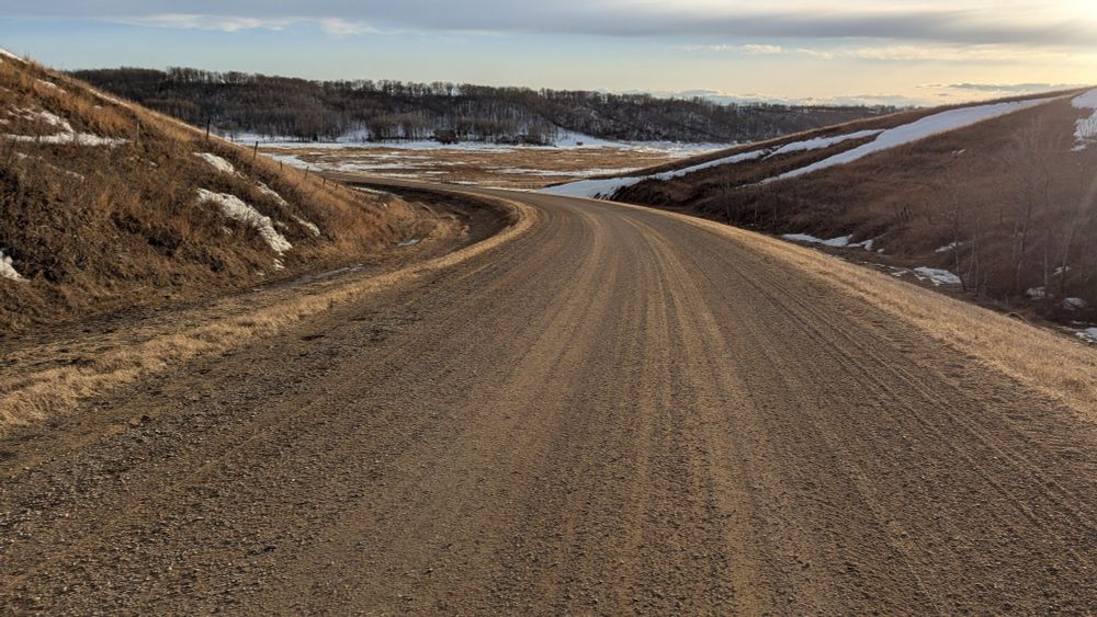 Gravel road descending into the valley along Pipestone Creek. There is still a fair bit of snow in the fields. 