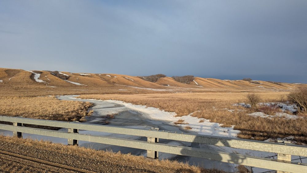 View to the east along Pipestone Creek with a view of the valley. The creek is mostly frozen. 
