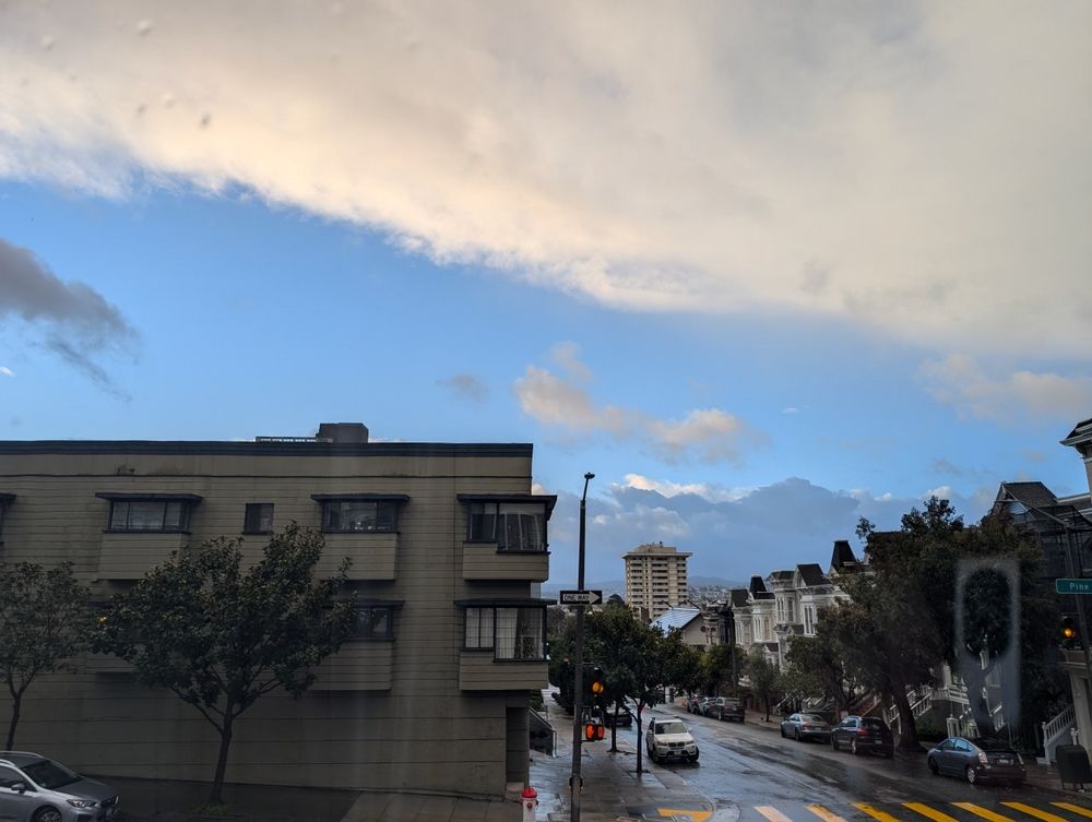 A view of the sky above San Francisco out my window. A break of blue is between dense thick clouds of starkly varying color. 