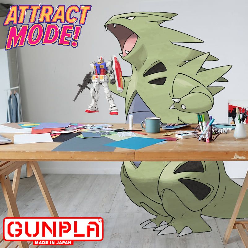 Sanjan (a real life tyranitar) holding a gunpla that they made from a table filled with art supplies. The logos "Attract Mode" for Lady Arcades and Gunpla are in the top left anf bottom left respectively