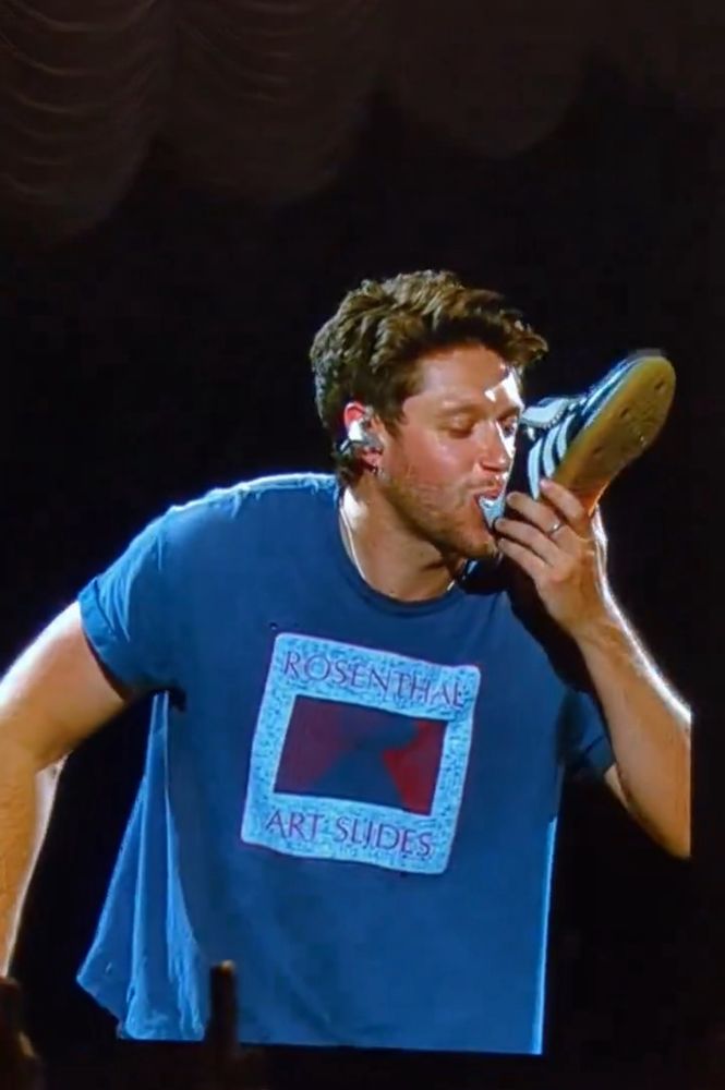 Niall in Australia does the local custom of drinking out of his show, a three striped Sambra or some similar design.

He wears a bit oversized blue t shirt with blue and magenta on the print, in a white larger rectangle that says Rosenthal Art Slides.