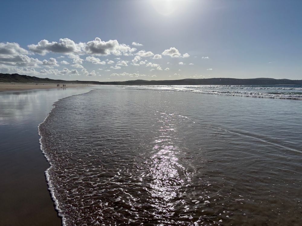 The beach, the sea, the sun shining on the sea, dunes in the far background. 
