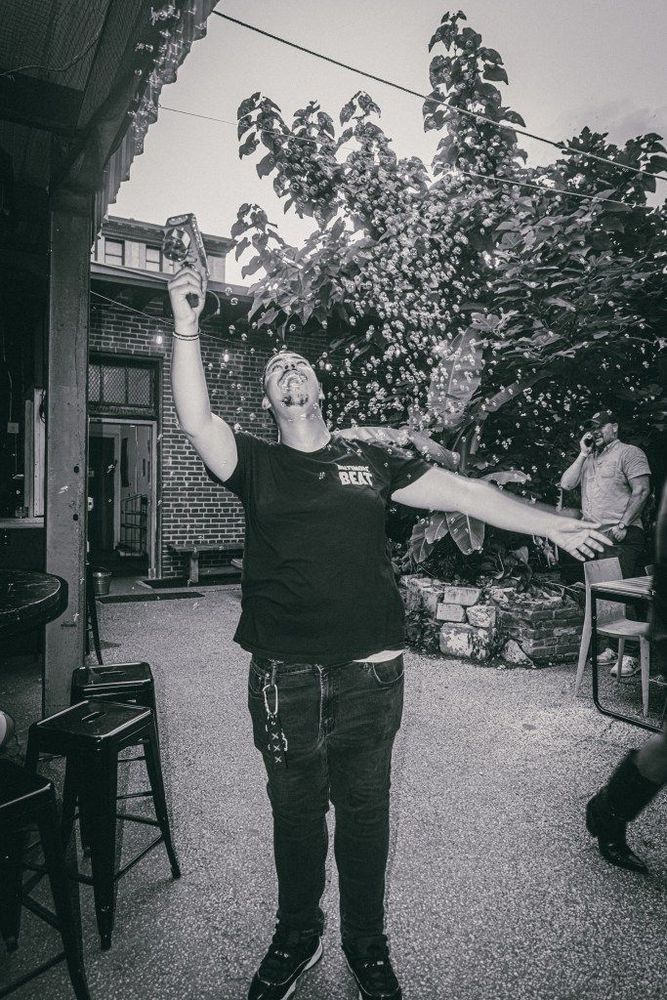 A young man laughs and shoots bubbles into the air with a bubble gun.