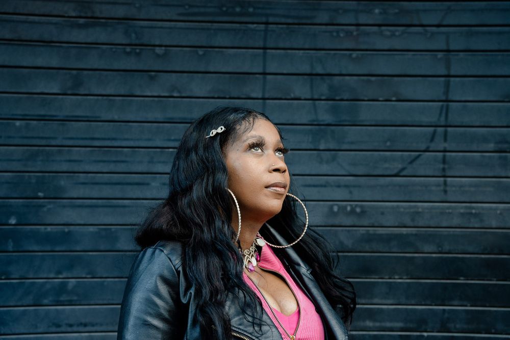 A photo of Tawanda Jones, a Black woman. She has long, wavy dark hair with sparkly clips in it. She wears a pink top under a black jacket.